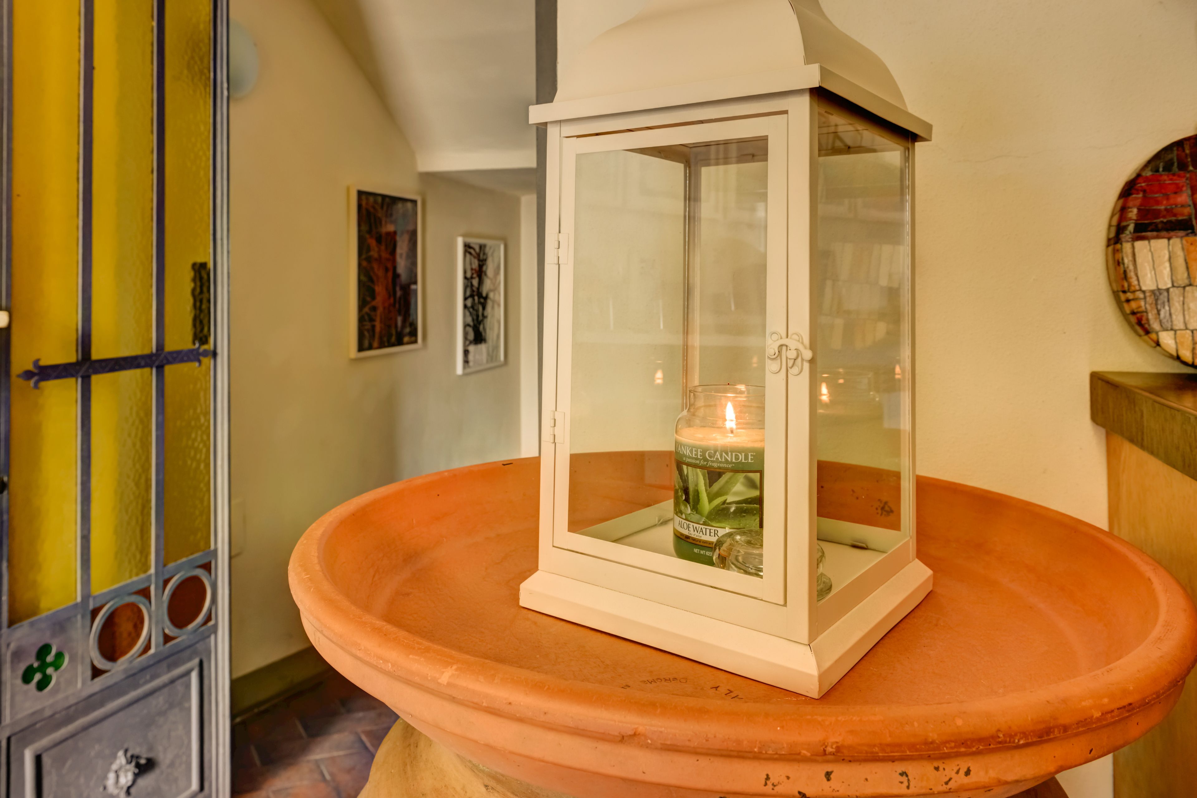 A white lantern with a candle inside, placed on a terracotta basin.