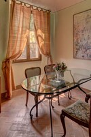 Un comedor con mesa de vidrio, dos sillas, un florero con flores y un cuadro en la pared.