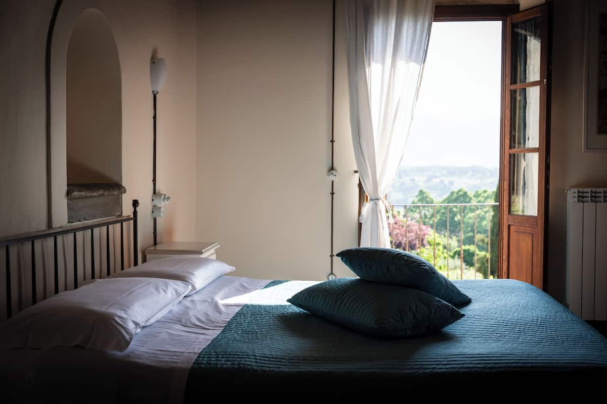 A bedroom with a bed, a window with curtains, a nightstand, and a lamp.