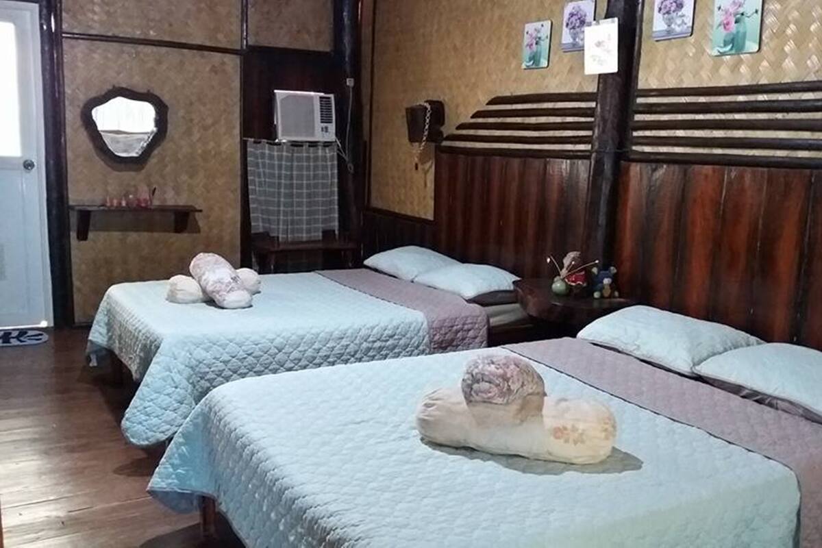 Une chambre d’hôtel avec deux lits, une tête de lit en bois, un miroir, un appareil de climatisation et une petite étagère ornée d’objets décoratifs.