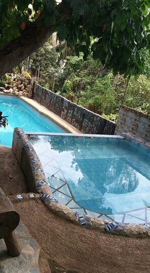 A swimming pool with a stone wall and tiled edge, surrounded by lush greenery. - Kopi Doki Guest Haus (Coron)
