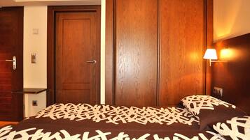 A hotel room with a bed, a wooden wardrobe, a nightstand, and a wall-mounted lamp.
