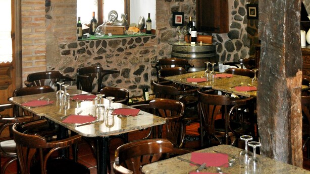 Een rustiek restaurantinterieur met stenen muren, houten balken en meerdere tafels en stoelen.