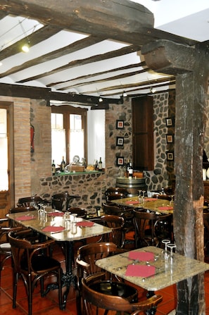 A rustic restaurant interior with stone walls, wooden beams, and multiple tables and chairs.