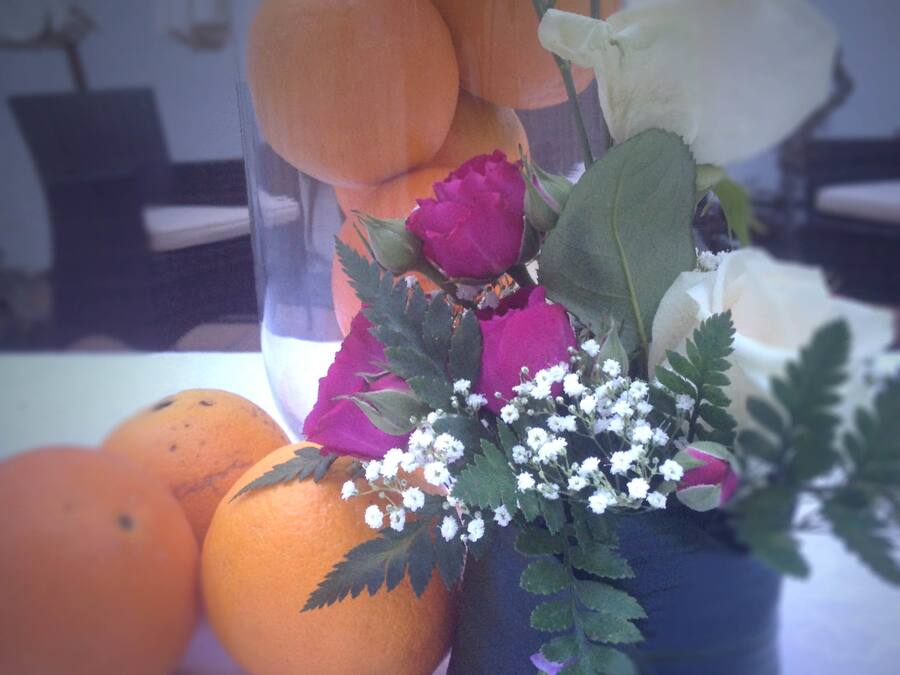 A clear glass vase with flowers and oranges on a table.