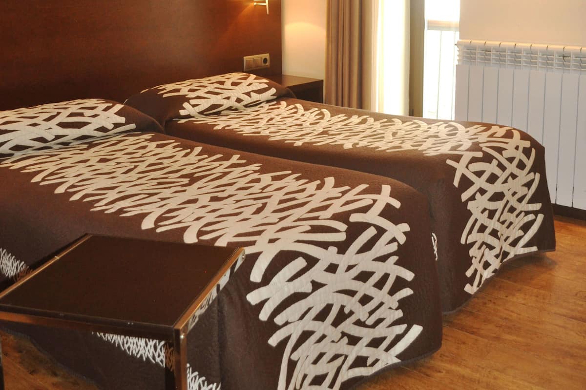 Habitación de hotel con dos camas, vigas de madera en el techo, una mesita de noche, una lámpara y una ventana con cortinas.