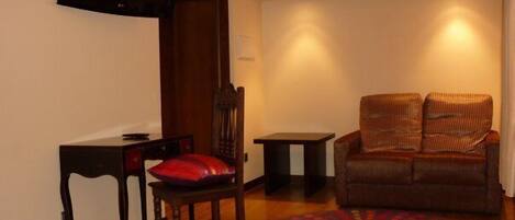 A hotel room with a bed, a desk with a chair, a television mounted on the wall, a brown sofa, and a colorful rug.