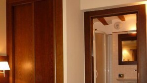 Een hotelkamer met een groot bed, houten balken in het plafond, een badkamer die zichtbaar is door een open deur, en een nachtkastje met een lamp.