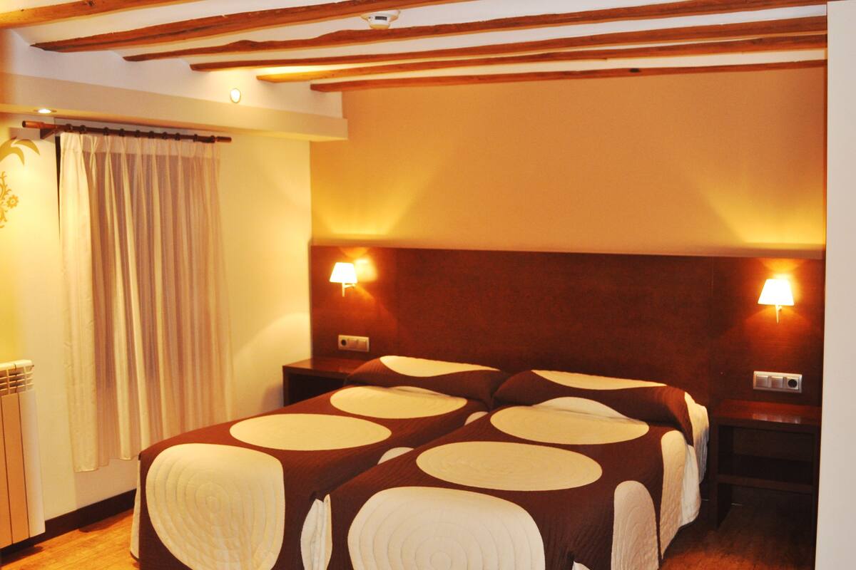 Habitación de hotel con una cama grande, dos lámparas de noche, un cabecero de madera y una cortina.