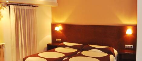 A hotel room with a large bed, two bedside lamps, a wooden headboard, and a curtain.