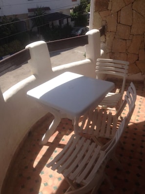 A small outdoor seating area with a white table and chairs, a stone wall, and a tiled floor. - Complexe Mouna Résidence Elachhab (M'diq)