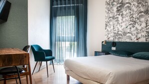 A modern hotel room with a wooden floor, a bed with white bedding, a blue chair, a small table, and a wall-mounted TV. - Grand Hôtel du Parc (Florac)