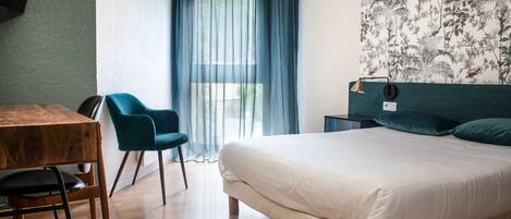 A modern hotel room with a wooden floor, a bed with white bedding, a blue chair, a small table, and a wall-mounted TV.