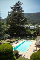 Piscina com espreguiçadeiras, cercada por gramados bem cuidados e árvores altas.