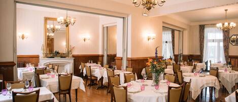 A dining area with multiple tables set for service, wooden chairs, and chandeliers.