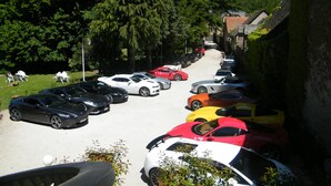 A parking lot with multiple cars parked in rows, surrounded by greenery and a building with a tiled roof. - Grand Hôtel du Parc (Florac)