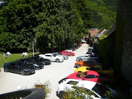 A parking lot with multiple cars parked in rows, surrounded by greenery and a building with a tiled roof.
