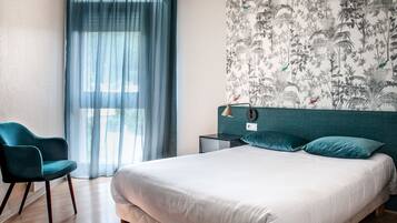 Un dormitorio con cama, una silla, una mesita de noche, una lámpara y una ventana con cortinas.