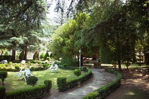 Um jardim bem cuidado com sebes aparadas, um caminho curvo e área de estar externa com cadeiras brancas.