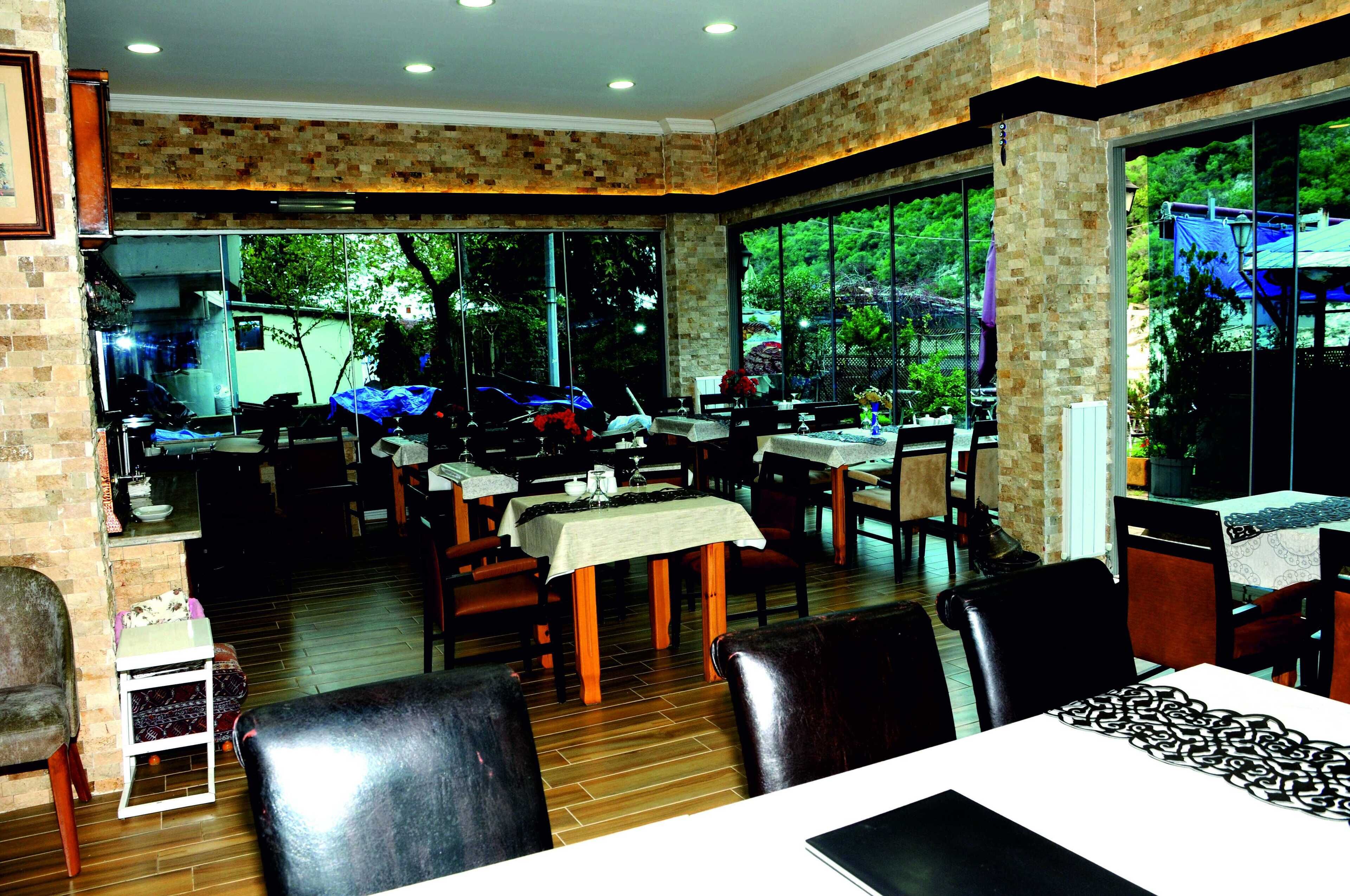 A restaurant with brick walls, large windows, and wooden flooring. Tables are set with white tablecloths and centerpieces.