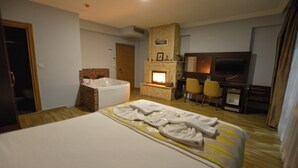 Quarto de hotel com uma cama grande, banheiro separado, lareira, televisão e escrivaninha.