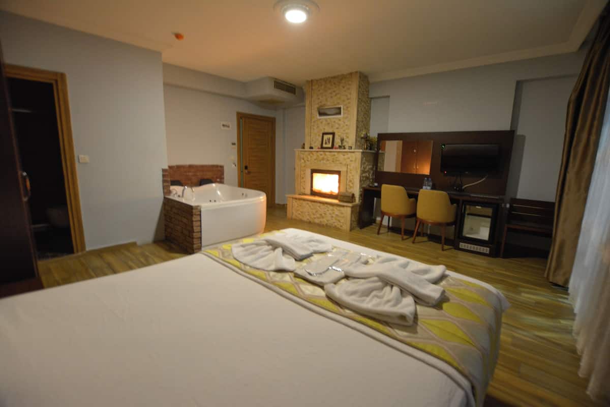 A hotel room with a large bed, a separate bathroom, a fireplace, a television, and a desk.