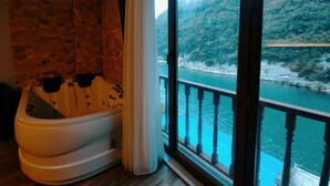 Quarto com uma grande janela com vista para um rio e colinas arborizadas.