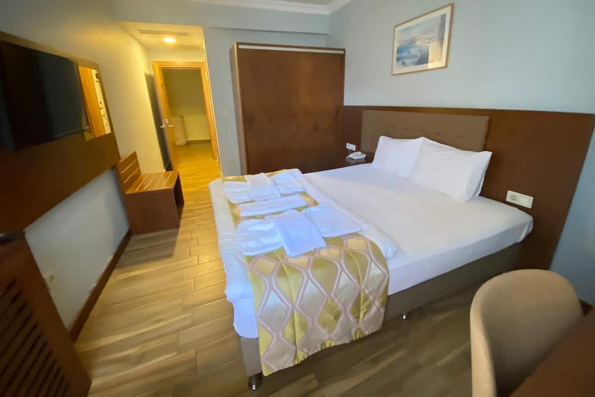 A hotel room with a large bed, a bedside table, a chair, a television, and a door leading to another room.