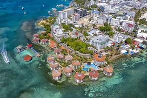 An aerial view of a coastal resort with multiple buildings, a marina, and clear blue waters.