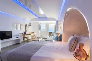 A modern hotel room with a large bed, a TV, a desk, and a view of the outdoors.