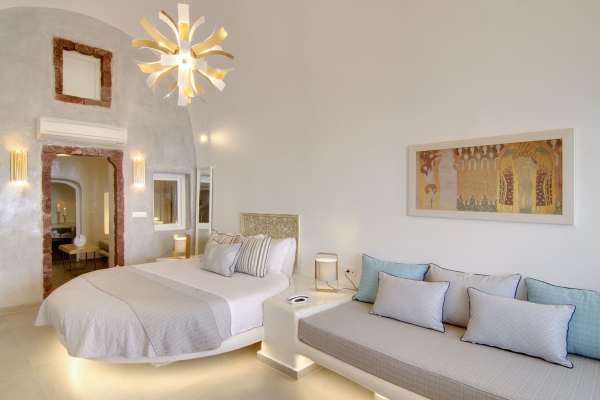A modern bedroom with a large bed, a sofa, a mirror, and a unique ceiling light fixture.