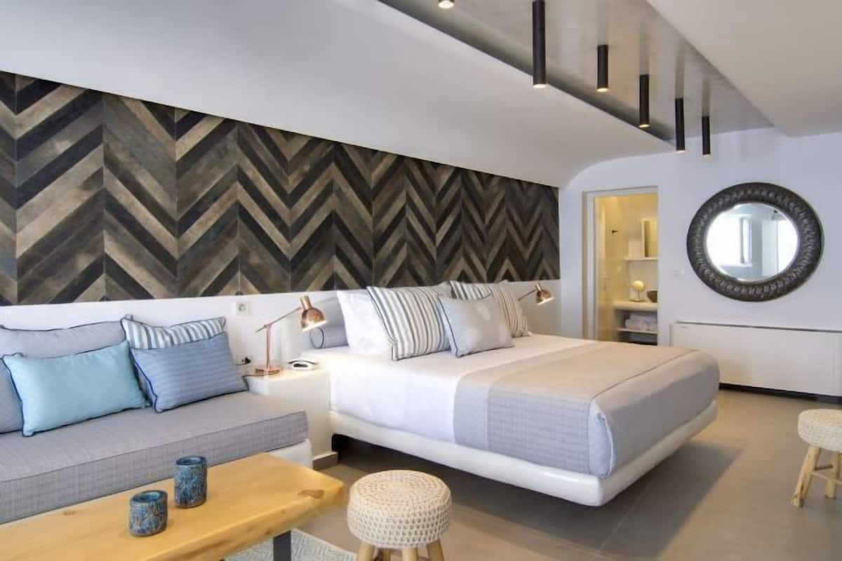 A modern bedroom with a bed, sofa, bedside tables, and a herringbone-patterned wall.