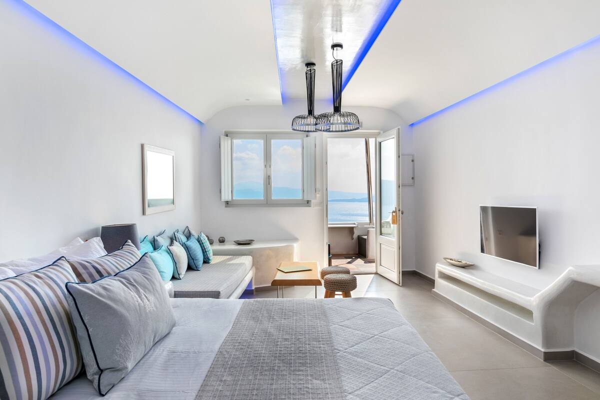 A modern living room with a sofa, a TV, and a view of the sea.