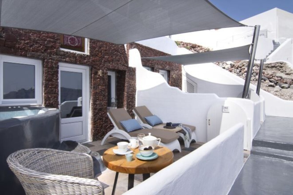 A modern outdoor seating area with a table set for two, a hot tub, and a stone wall.