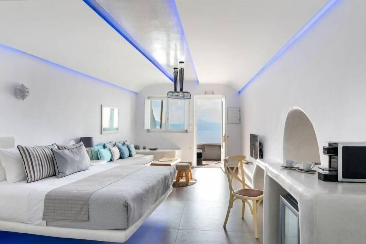 A modern bedroom with a bed, seating area, and a kitchenette.