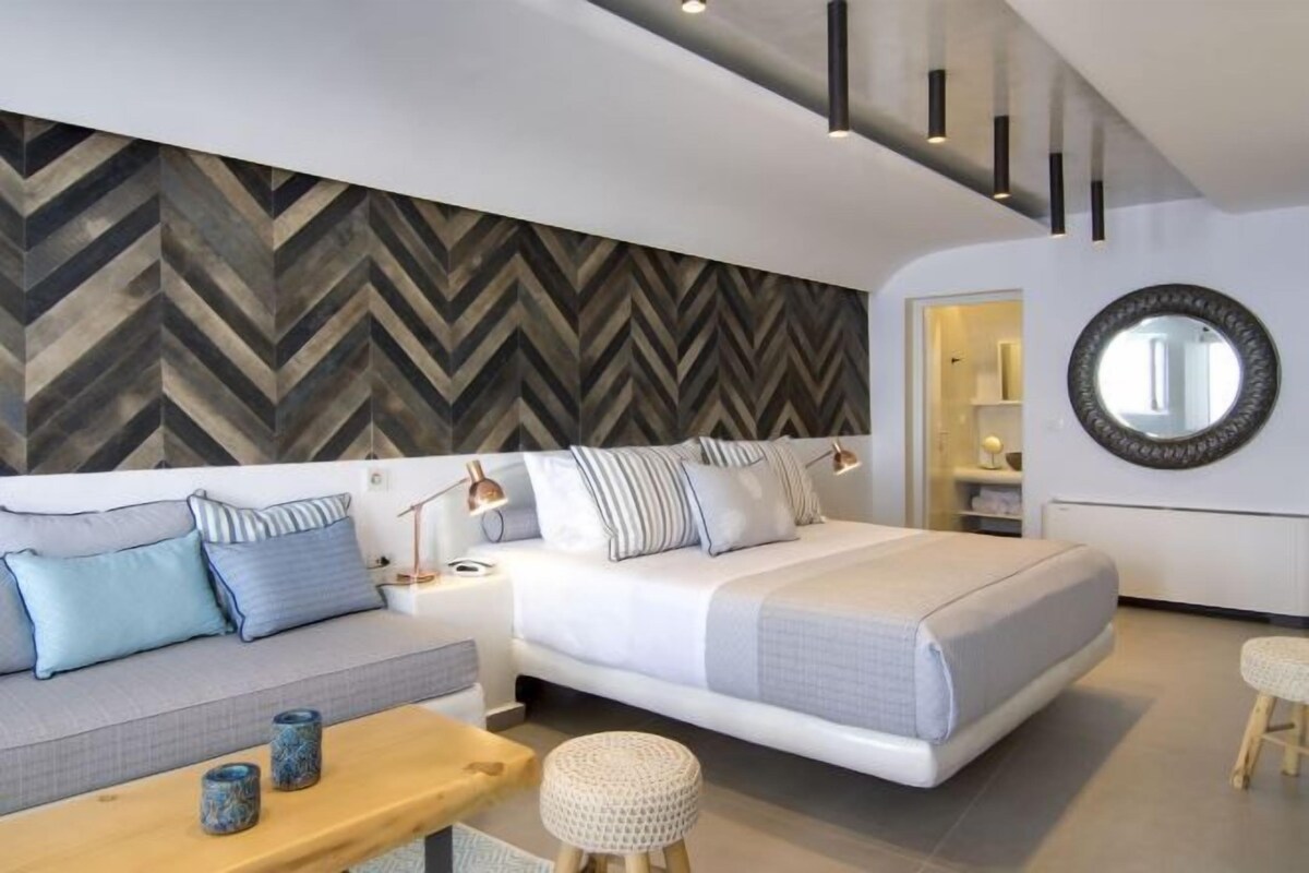 Ein modernes Schlafzimmer mit Bett, Sofa, Nachttischen und einer Wand mit Fischgrätmuster.