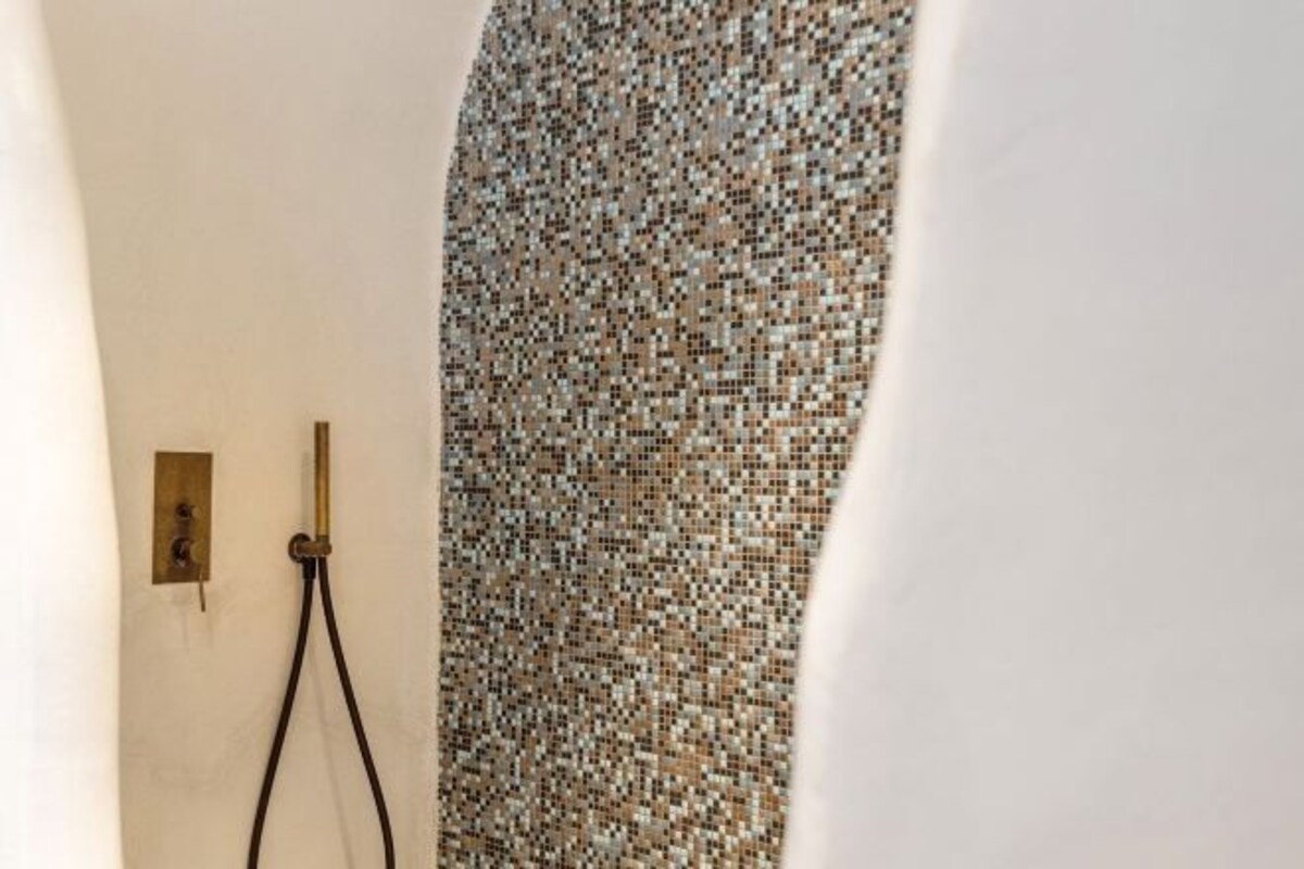 A bathroom with a mosaic wall, a shower area, and a brass fixture.
