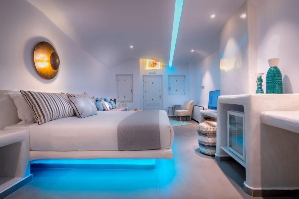 A modern hotel room with a bed, seating area, and a television.