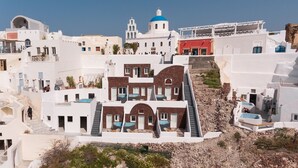 Edifici blanc amb una cúpula blava i una porta vermella, envoltat d'altres edificis blancs i un pendent rocós.
