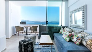 A modern living room with a sofa, chairs, a coffee table, and a large window offering a view of the sea. - Santorini Secret Premium (Santorini)