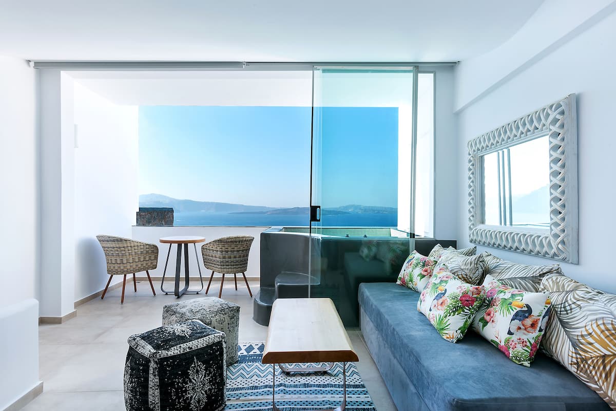 A modern living room with a sofa, chairs, a coffee table, and a large window offering a view of the sea.
