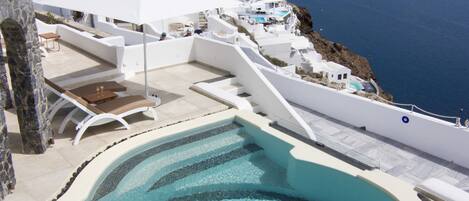 A pool with a spiral design, white buildings, and a view of the sea.