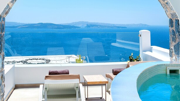 A sunlit terrace with a view of the sea, a hot tub, and lounge chairs. - Santorini Secret Premium (Santorini)