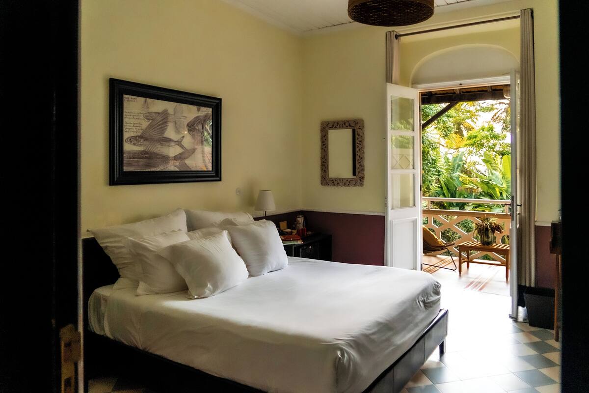 A neatly made bed with white linens in a room with a large window and a door leading to a balcony.
