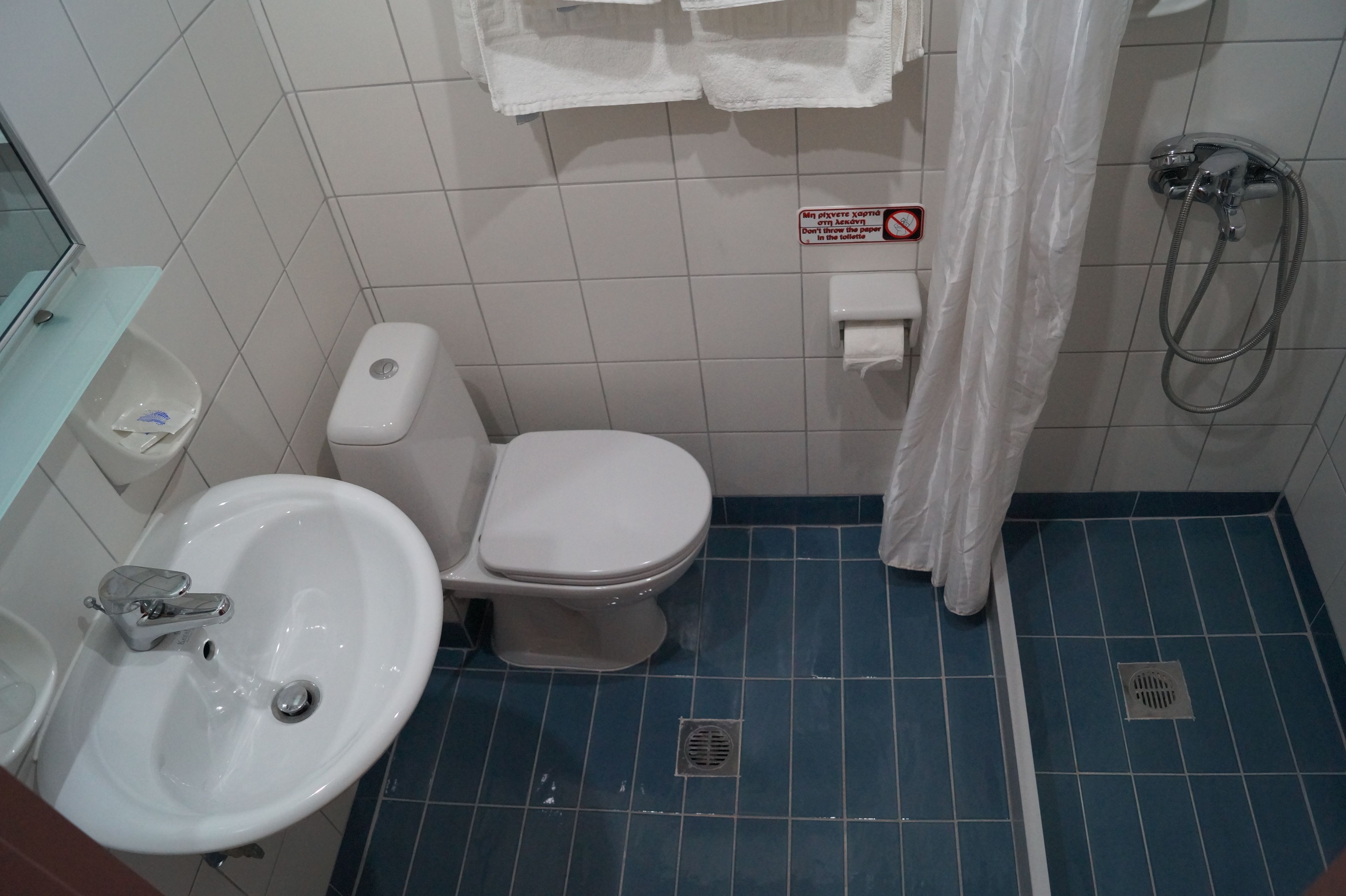 A small bathroom with a toilet, bidet, and sink. There is a sign prohibiting paper disposal in the toilet.