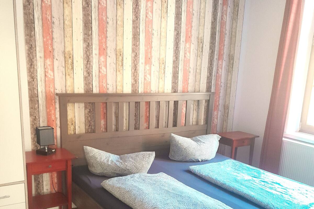A bedroom with a wooden headboard, a bed with patterned bedding, a nightstand, and a dresser.