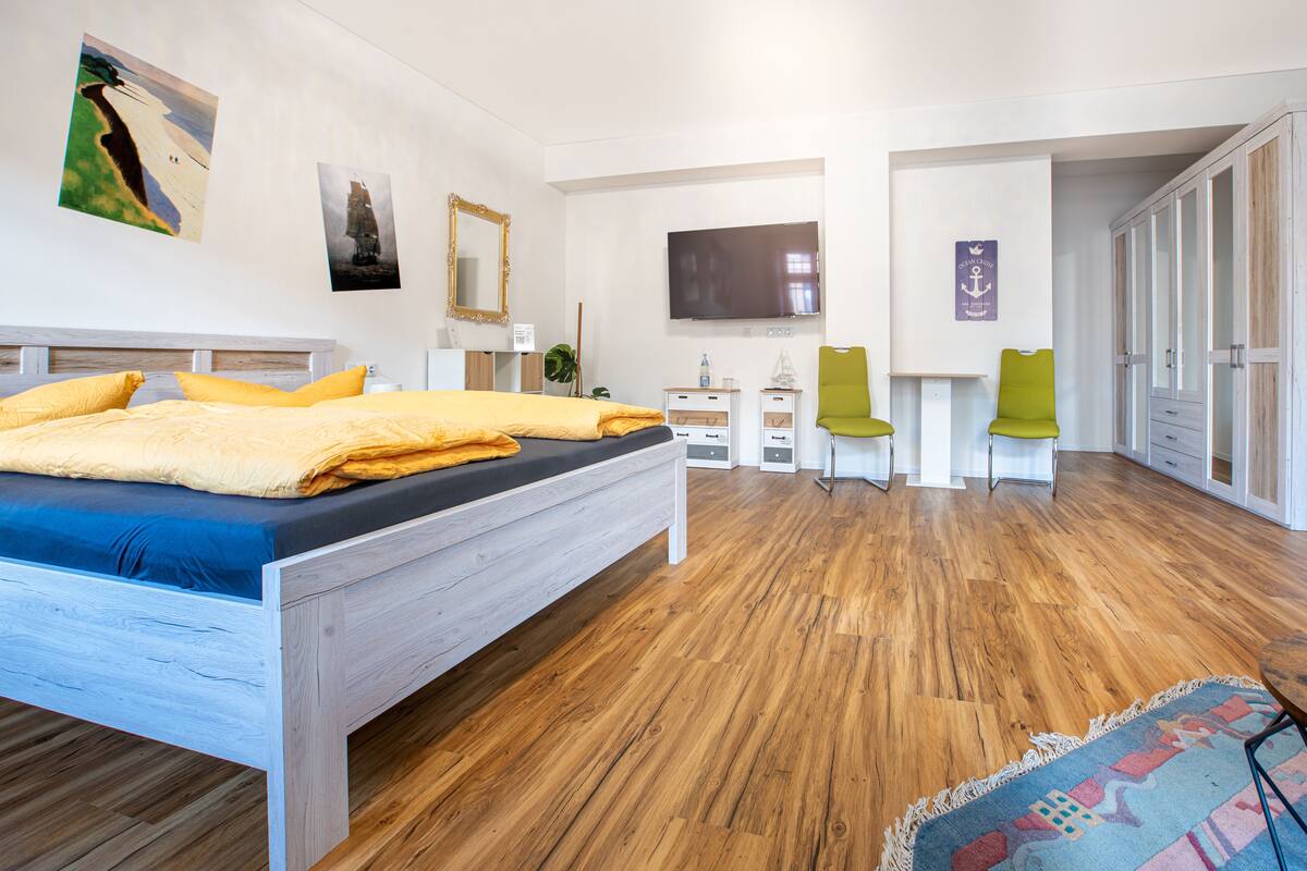 A bedroom with a wooden bed, a flat-screen TV, a mirror, and a green chair.