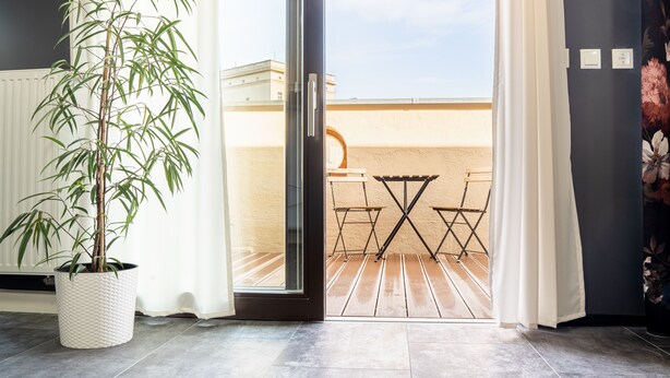Habitación con una planta de bambú en maceta, una puerta corrediza de vidrio que da a un patio exterior con una mesa y sillas de madera.