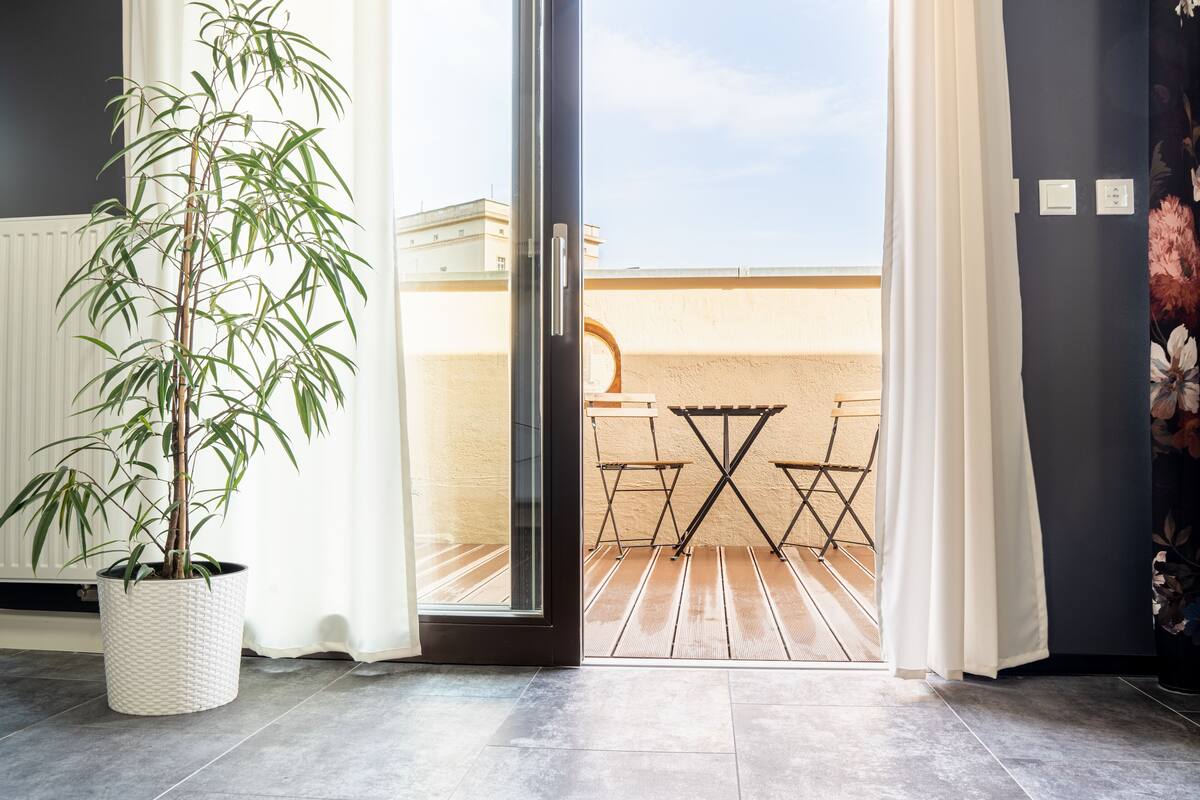 A room with a potted bamboo plant, a sliding glass door leading to an outdoor patio with a wooden table and chairs.