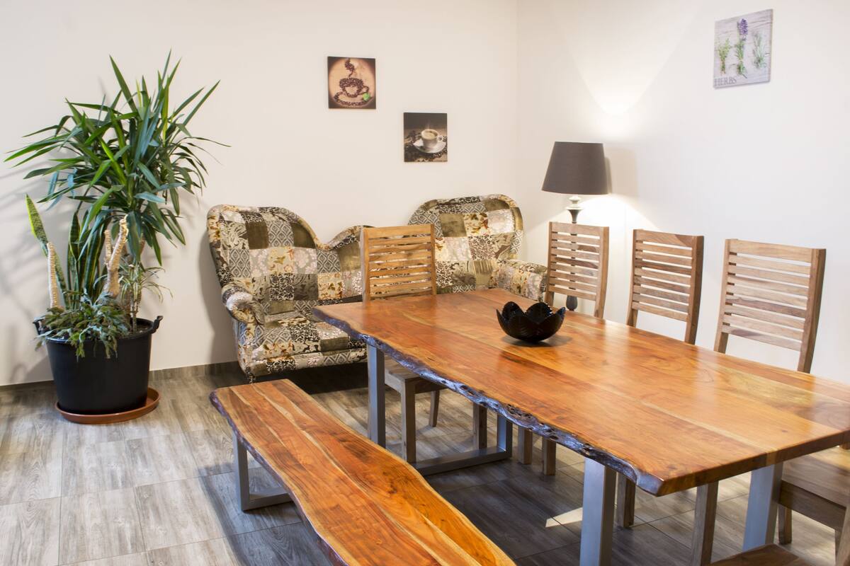 A dining area with a wooden table, benches, patterned chairs, a potted plant, and wall art.